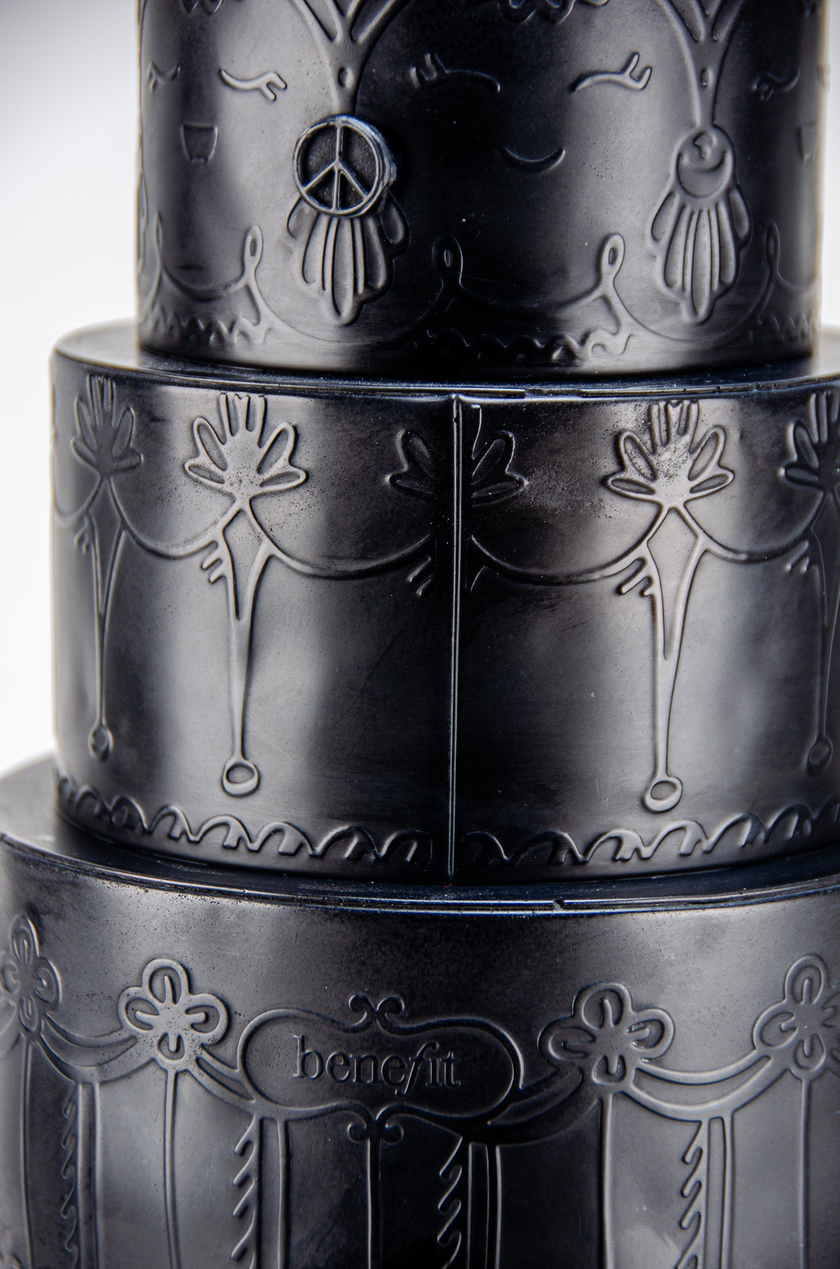 Small detailed view of tall dark charcoal sculpture of Marie Antoinette wearing a giant three-layered cake with charcoal Macrons on top of her head.